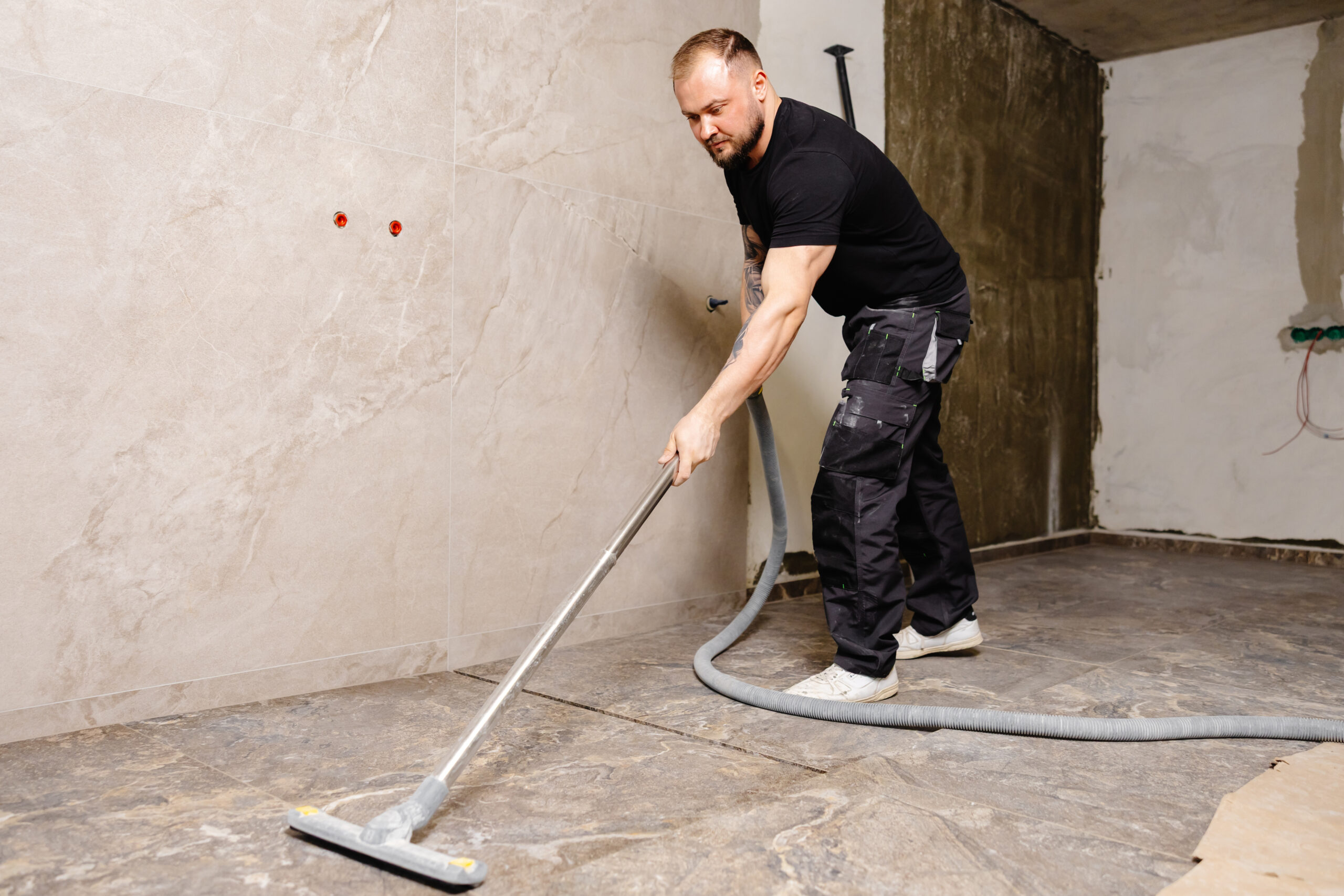 Construction worker using industrial vacuum cleaner to remove dust and debris after laying tiles in modern bathroom