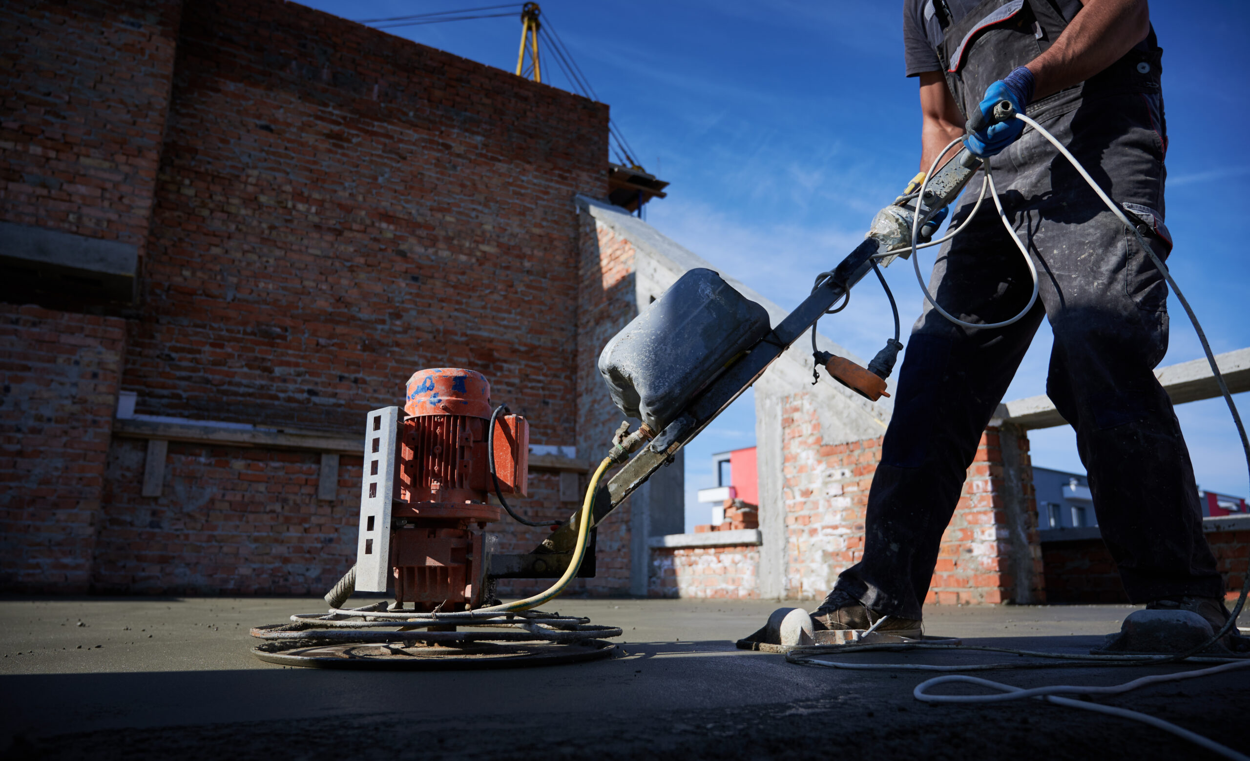 Cropped picture of man laborer in work overalls using power trowel machine while screeding floor in new building. Male worker finishing concrete surface with troweling machine at construction site.