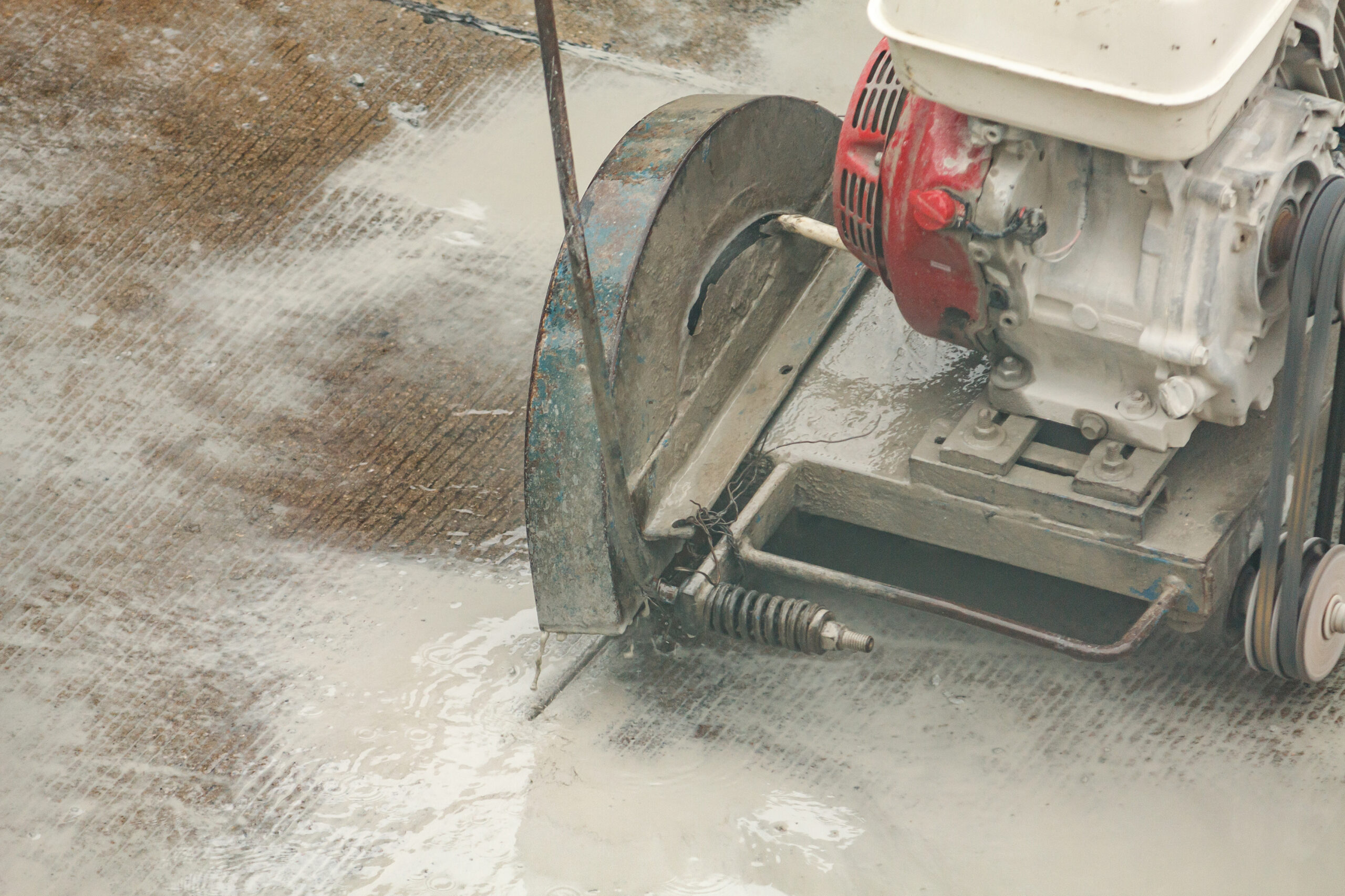 Worker using diamond saw blade machine cutting concrete road at construction site